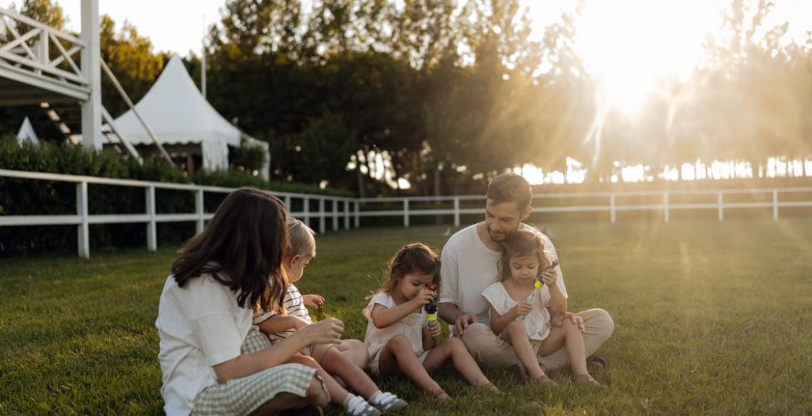 Family sitting on grass enjoying leisure time outdoors, with sun setting in the background.