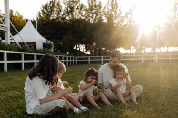 Family sitting on grass enjoying leisure time outdoors, with sun setting in the background.
